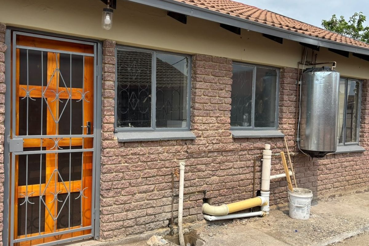 Rear exterior view of the property featuring exposed brickwork, a security gate, and external geyser installation.