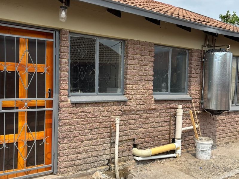 Rear exterior view of the property featuring exposed brickwork, a security gate, and external geyser installation.