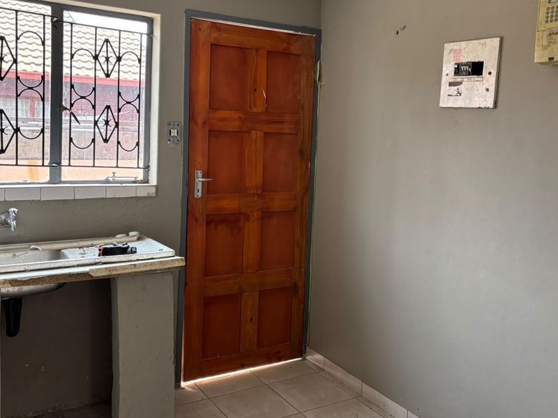 A functional scullery or utility area featuring a stainless steel sink, tiled flooring, and direct access to the exterior via a timber door.