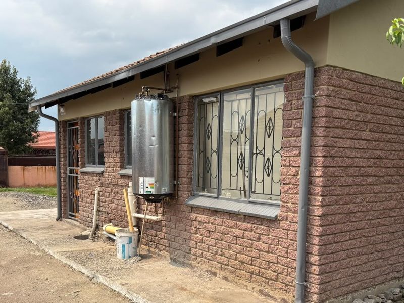 Rear exterior view of the house featuring exposed brickwork, an external electric geyser, and security bars on the windows.