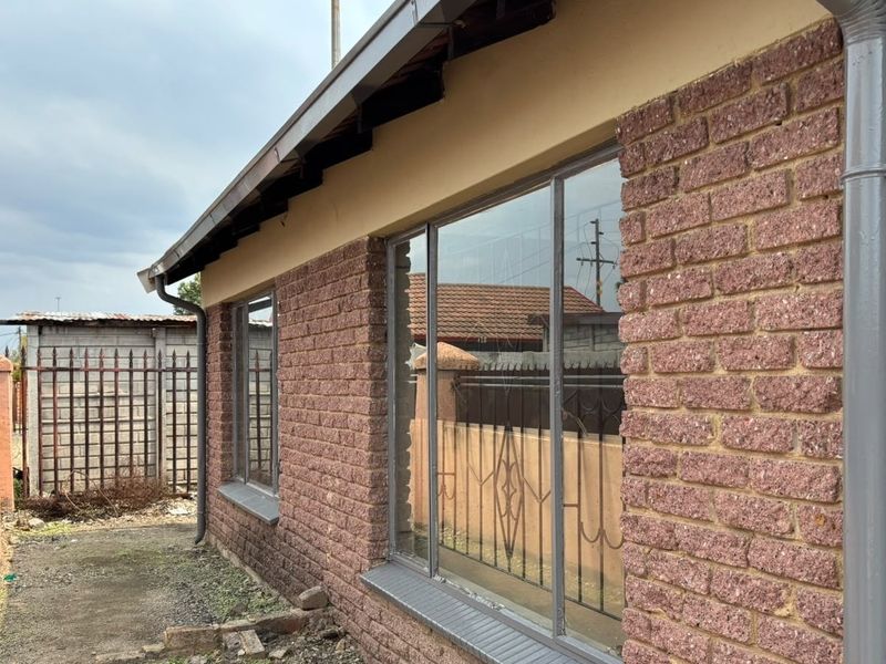 Side view of the property featuring face brick exterior, metal window frames with security bars, and functional guttering system.
