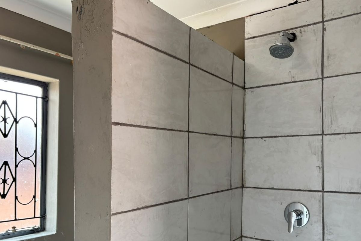 A bathroom under renovation featuring a tiled shower enclosure with installed fixtures and a window with a security gate.