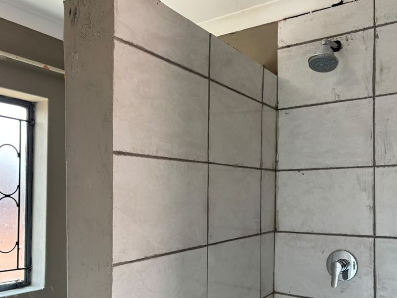 A bathroom under renovation featuring a tiled shower enclosure with installed fixtures and a window with a security gate.