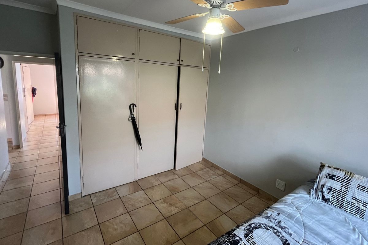 A bedroom featuring built-in cupboards, a ceiling fan, and tiled flooring, with an adjacent hallway visible.
