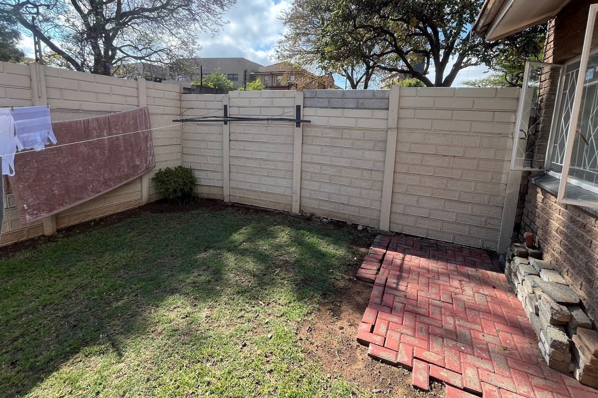 A small rear courtyard featuring a brick paved patio area, a lawn, and a precast concrete boundary wall with security window bars.
