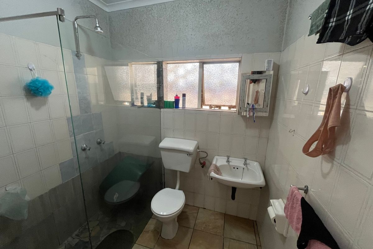 A compact bathroom featuring a glass-enclosed shower, wall-mounted basin, and toilet, with tiled finishes and a window for natural light.