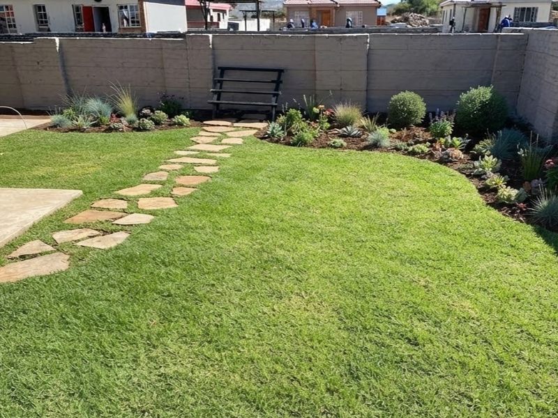 A well-maintained private garden featuring a stone pathway, manicured lawn, and landscaped garden beds enclosed by a concrete boundary wall.
