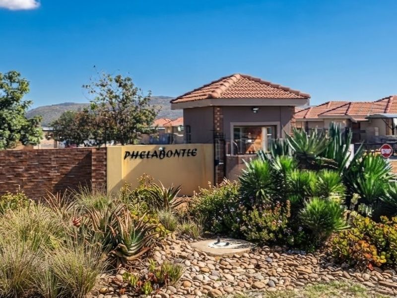Entrance view of Phelabontle estate featuring a security guard house, brick boundary wall, and well-maintained landscaped garden.