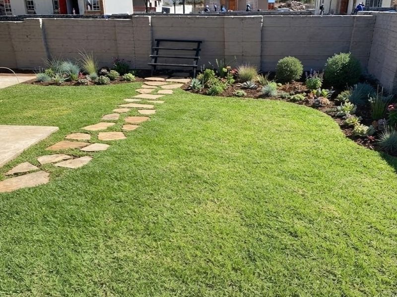 A well-maintained private garden featuring a stone paver pathway, lush lawn, and established garden beds enclosed by a perimeter boundary wall.