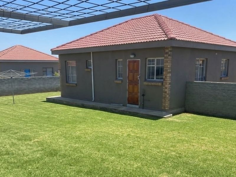 A view of the rear exterior of the house featuring a well-maintained lawn, brick boundary walls, and a tiled roof structure.