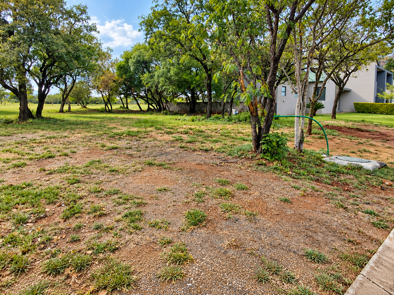 A spacious, open garden area featuring mature trees, concrete kerbing, and natural landscaping, offering potential for further development or garden enhancement.