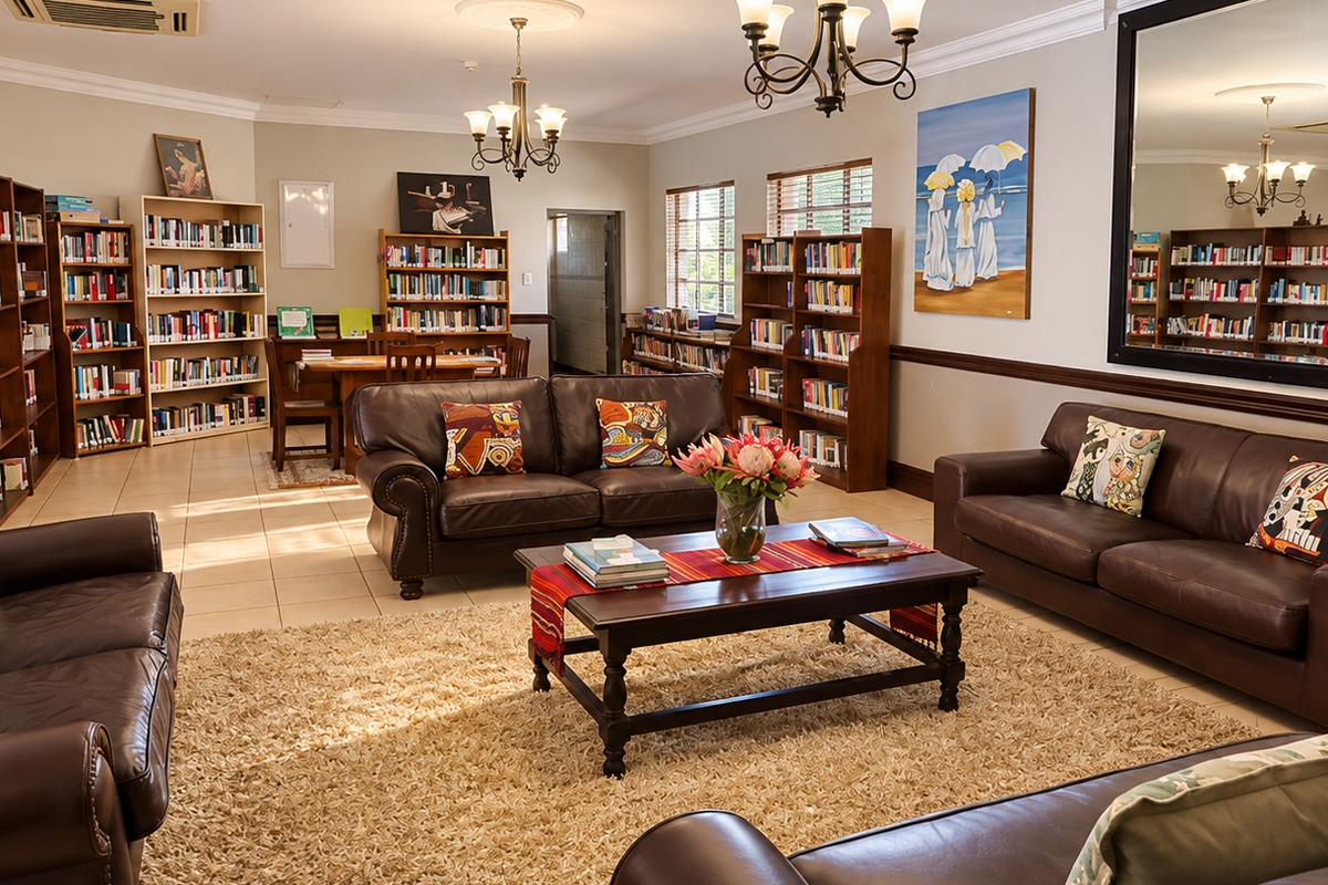 Spacious living area featuring extensive built-in library shelving, tiled flooring, crown molding, and a large wall mirror, creating a comfortable and functional communal space.