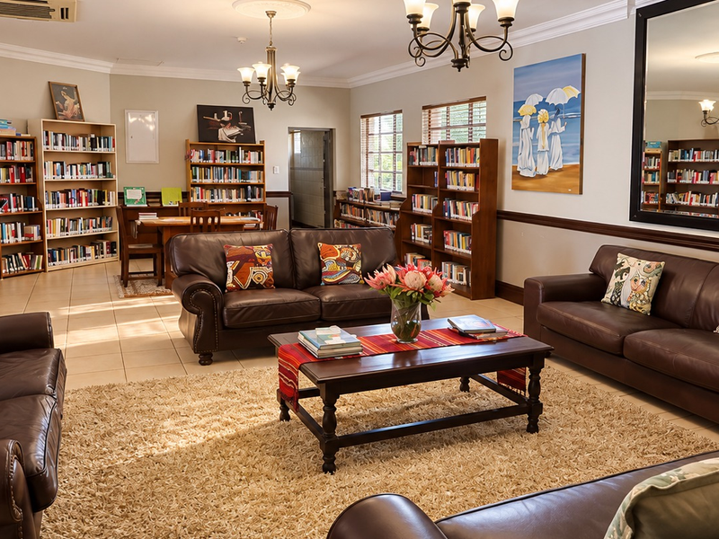 Spacious living area featuring extensive built-in library shelving, tiled flooring, crown molding, and a large wall mirror, creating a comfortable and functional communal space.