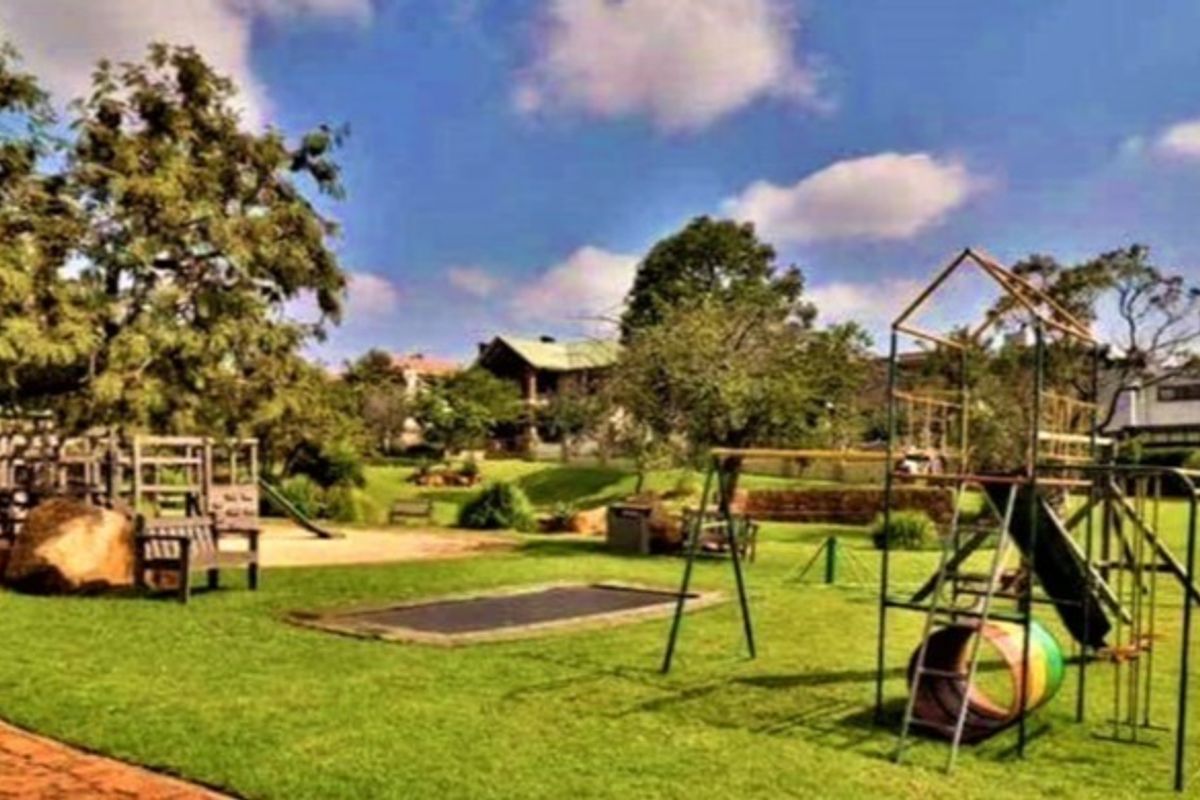 A spacious, well-maintained garden featuring a large lawn, mature trees, and integrated playground equipment including a trampoline and climbing structures.