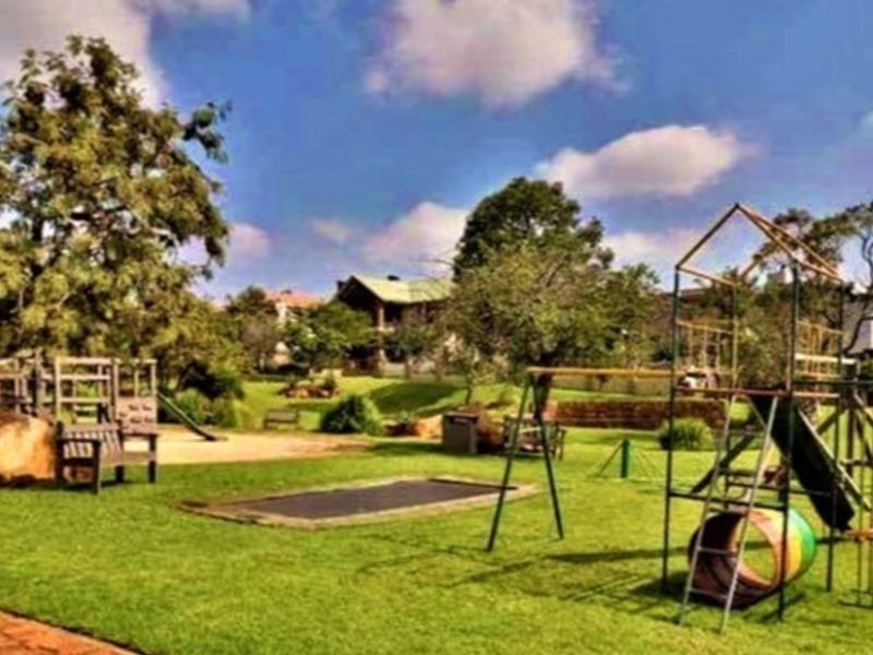 A spacious, well-maintained garden featuring a large lawn, mature trees, and integrated playground equipment including a trampoline and climbing structures.