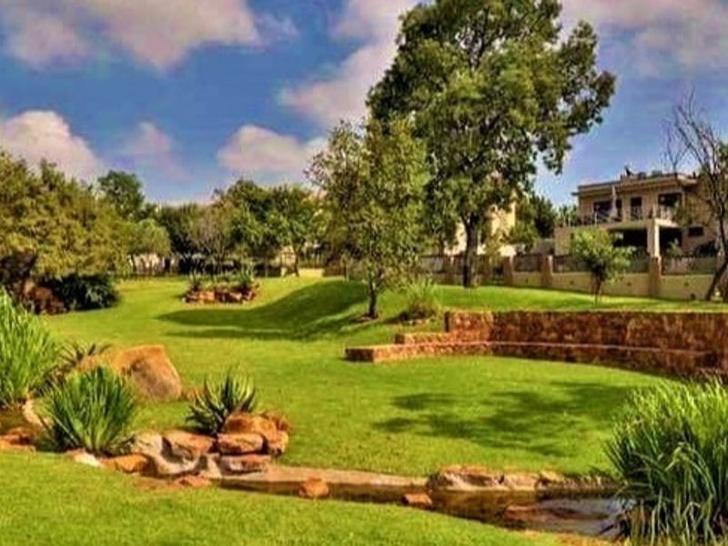 A spacious, well-maintained garden featuring a stone retaining wall, manicured lawn, and a natural stone water feature with the main residence in the background.