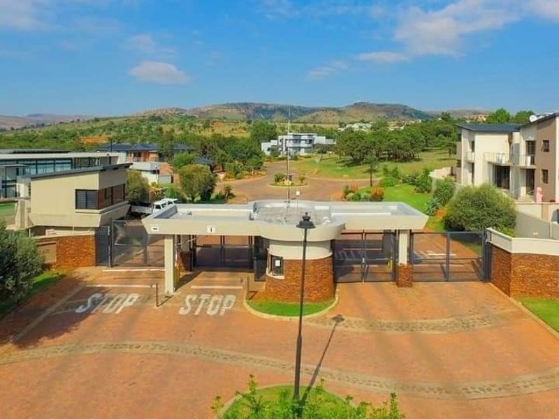 Aerial view of the secure estate entrance featuring a modern gatehouse, paved driveway, and well-maintained perimeter walls with landscaped surroundings.