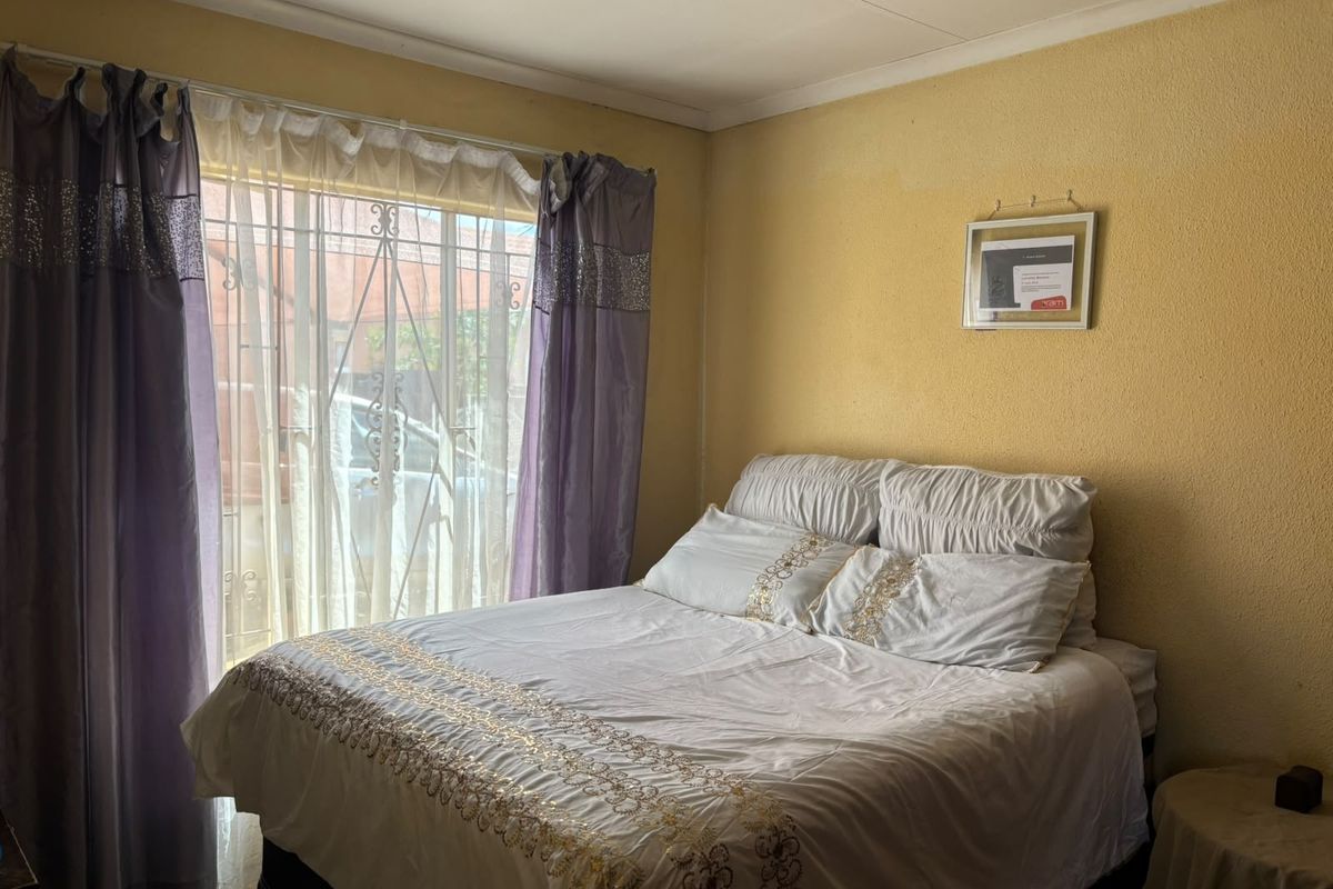 A bedroom featuring a window with a security gate. The room requires cosmetic updates to the wall finishes to improve its overall condition.