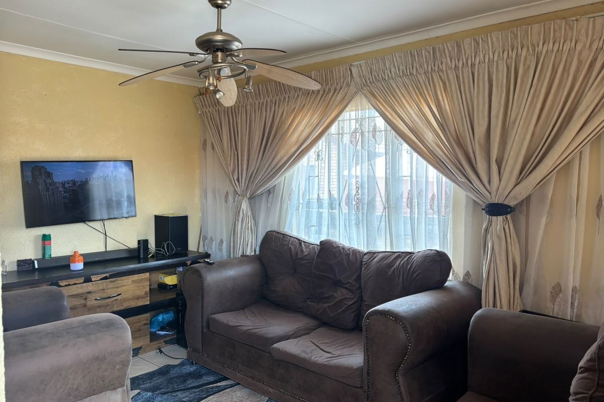 A living room featuring a ceiling fan, tiled flooring, and large window treatments, providing a functional space for relaxation.
