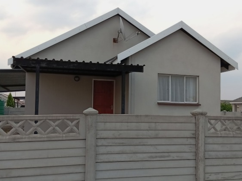 Front elevation of a single-story house featuring a gabled roof, attached carport, and a precast concrete boundary wall.