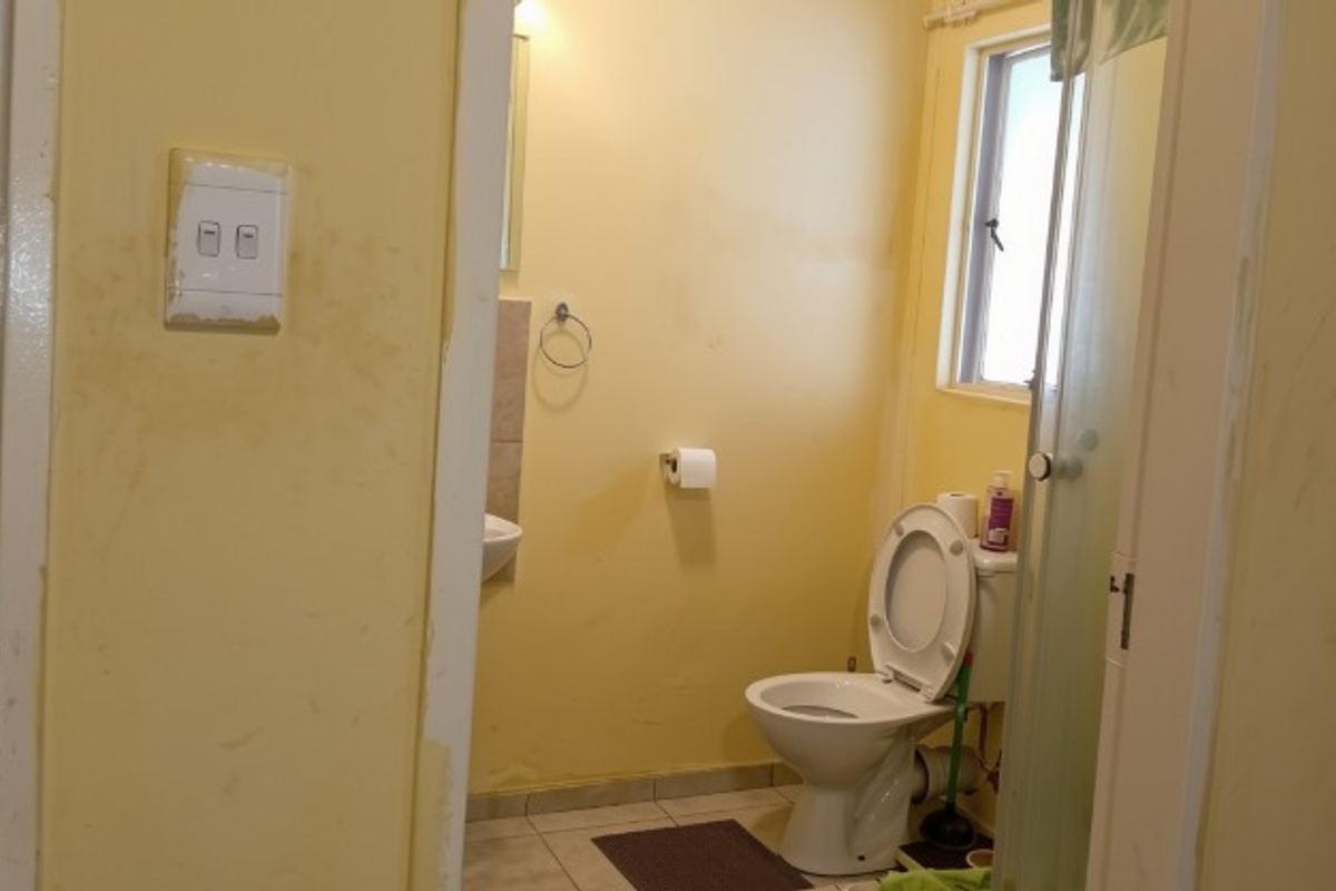 A functional bathroom featuring a toilet, shower enclosure, and tiled flooring, currently requiring cosmetic updates to the wall finishes.