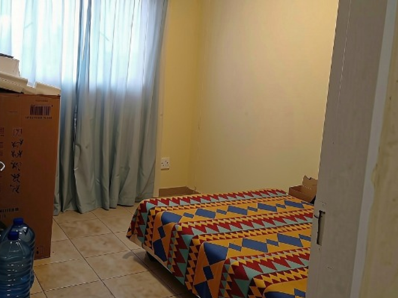 A simple bedroom featuring tiled flooring and a window with curtains, viewed from the doorway.