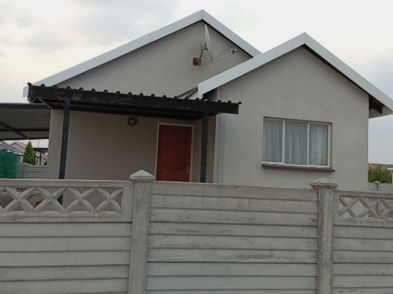 Front view of a single-story house featuring a gabled roof, a covered carport, and a precast concrete boundary wall.