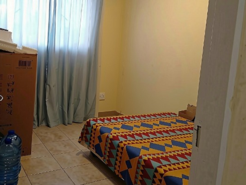 A standard bedroom featuring tiled flooring and window curtains, viewed from the doorway.