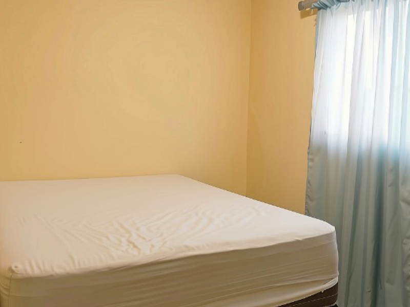 A simple bedroom featuring plain walls and a window with a curtain rod.