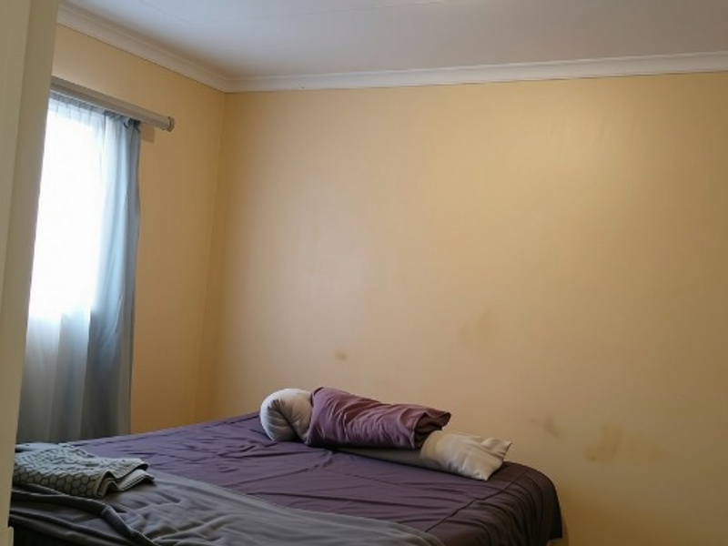 A bedroom featuring neutral wall finishes and a window with curtain track, requiring cosmetic updates to address wall staining and general wear.