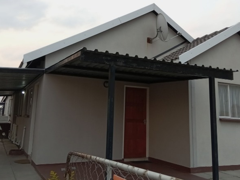 Front elevation of a single-story house featuring a covered carport, paved driveway, and a timber entrance door.