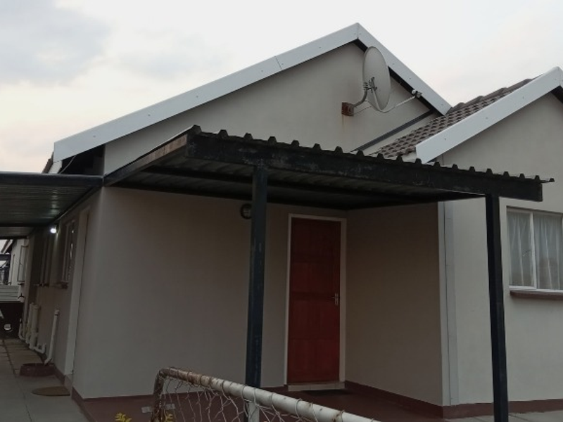 Front exterior view of a single-story house featuring a paved driveway, attached carport, and tiled roof structure.
