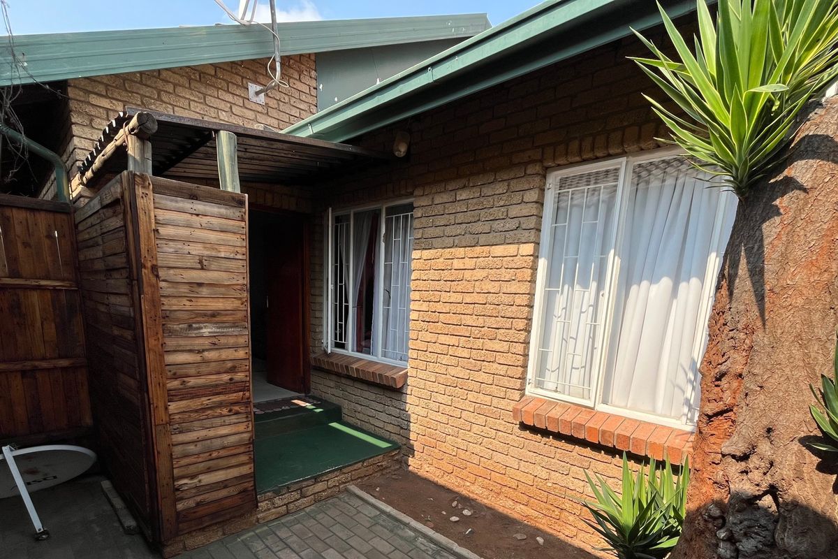 Rear exterior view of the townhouse featuring face brick walls, security window bars, and a small paved entrance area with a timber privacy screen.