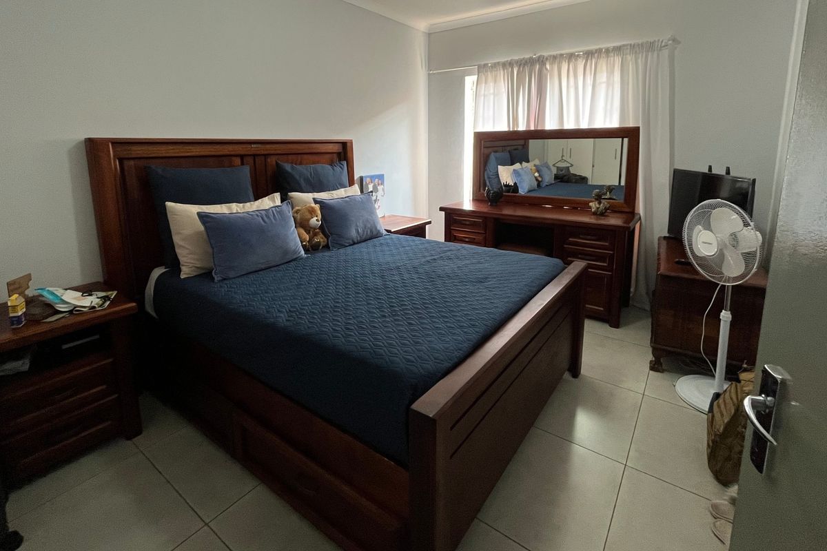 A spacious bedroom featuring neutral tiled flooring and large windows with installed curtain tracks, providing a functional and well-lit living space.