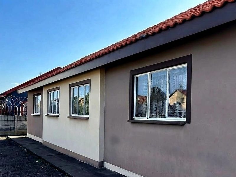 Rear exterior view of the house featuring a terracotta tiled roof, painted exterior walls, and aluminium window frames with a concrete boundary wall.