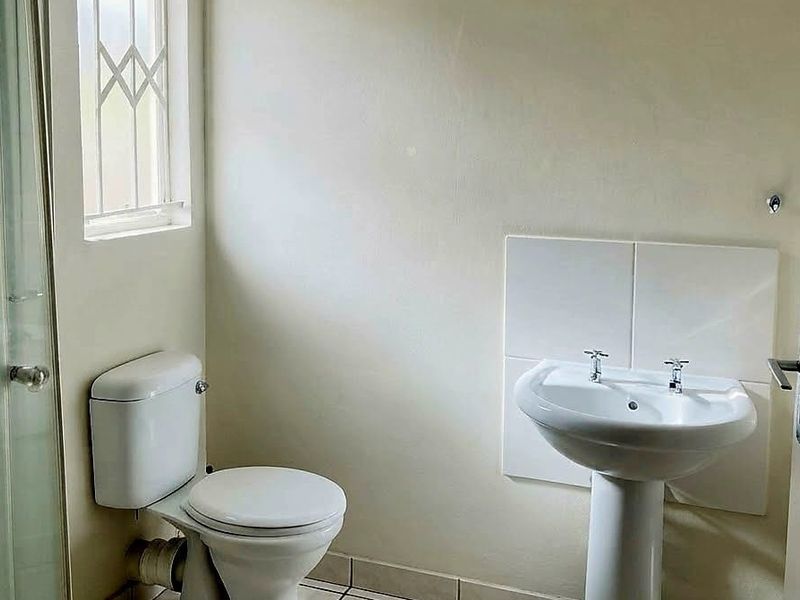 A functional bathroom featuring a pedestal basin, toilet, and a glass shower enclosure with tiled flooring.