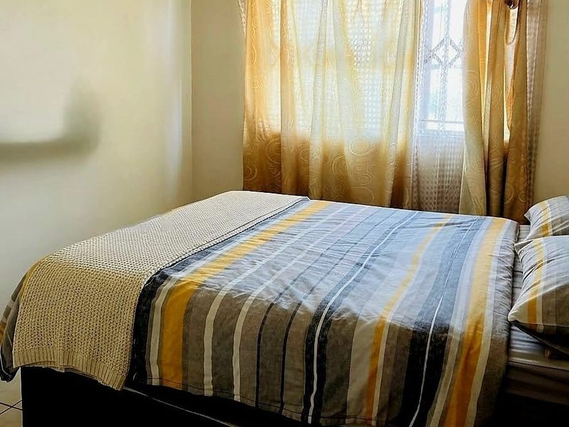 A standard bedroom featuring tiled flooring and a window fitted with security bars.