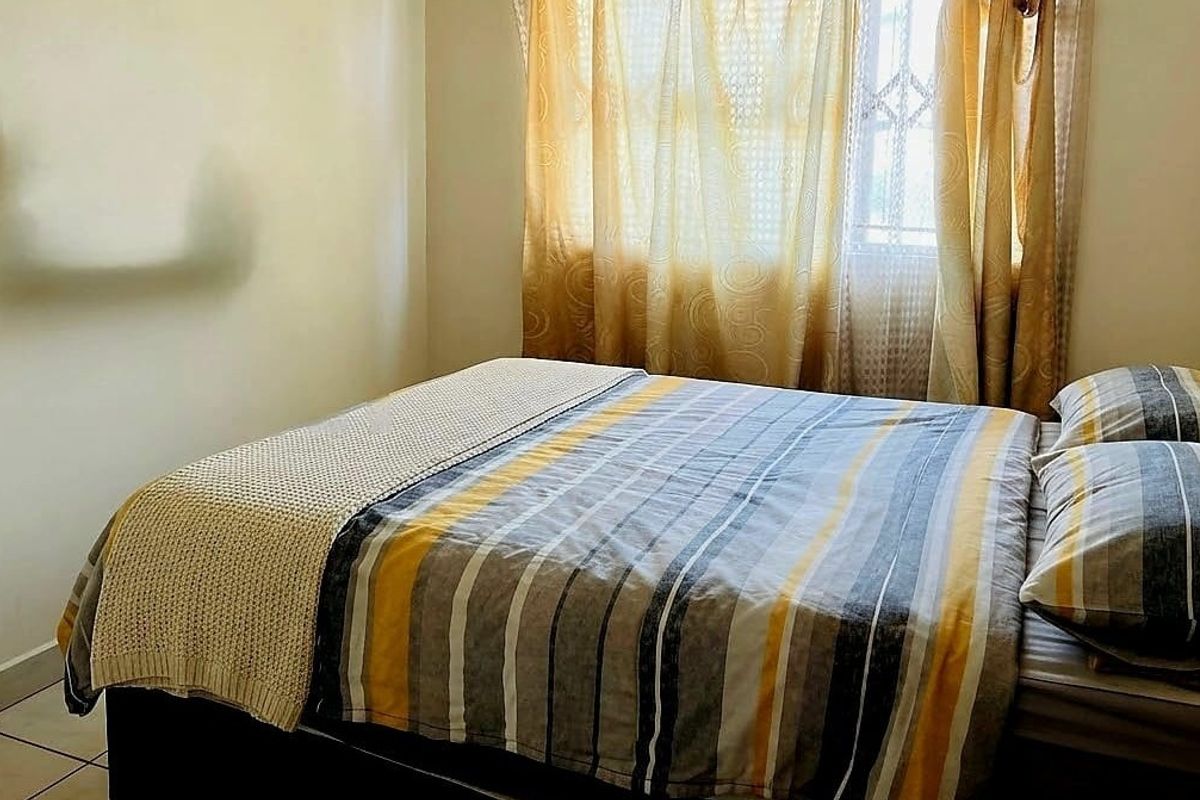 A standard bedroom featuring tiled flooring and a window fitted with security bars.