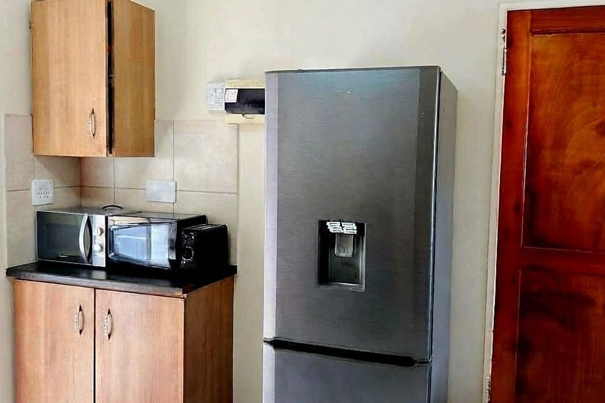 A compact kitchen area featuring laminate cabinetry, tiled splashback, and a dark countertop, providing functional storage and preparation space.