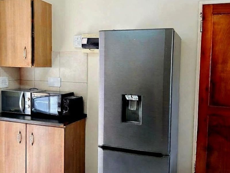 A compact kitchen area featuring laminate cabinetry, tiled splashback, and a dark countertop, providing functional storage and preparation space.