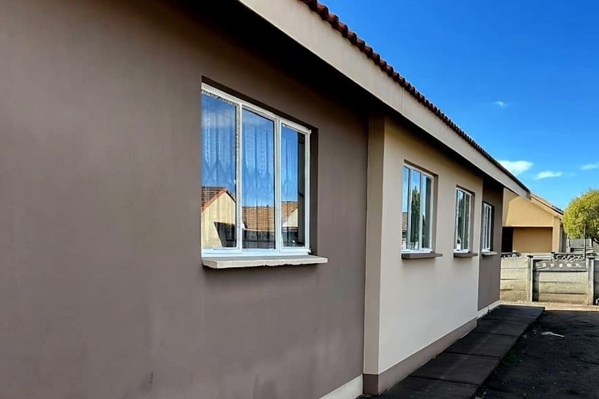 A view of the rear exterior elevation featuring a tiled roof, modern aluminium window frames, and a paved pathway along the side of the house.