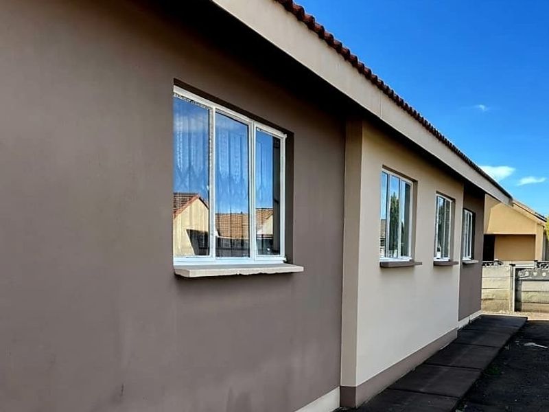 A view of the rear exterior elevation featuring a tiled roof, modern aluminium window frames, and a paved pathway along the side of the house.