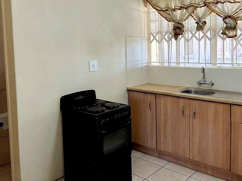 A functional kitchen featuring wood-look cabinetry, a stainless steel sink, and a freestanding stove, with tiled flooring and security bars on the window.