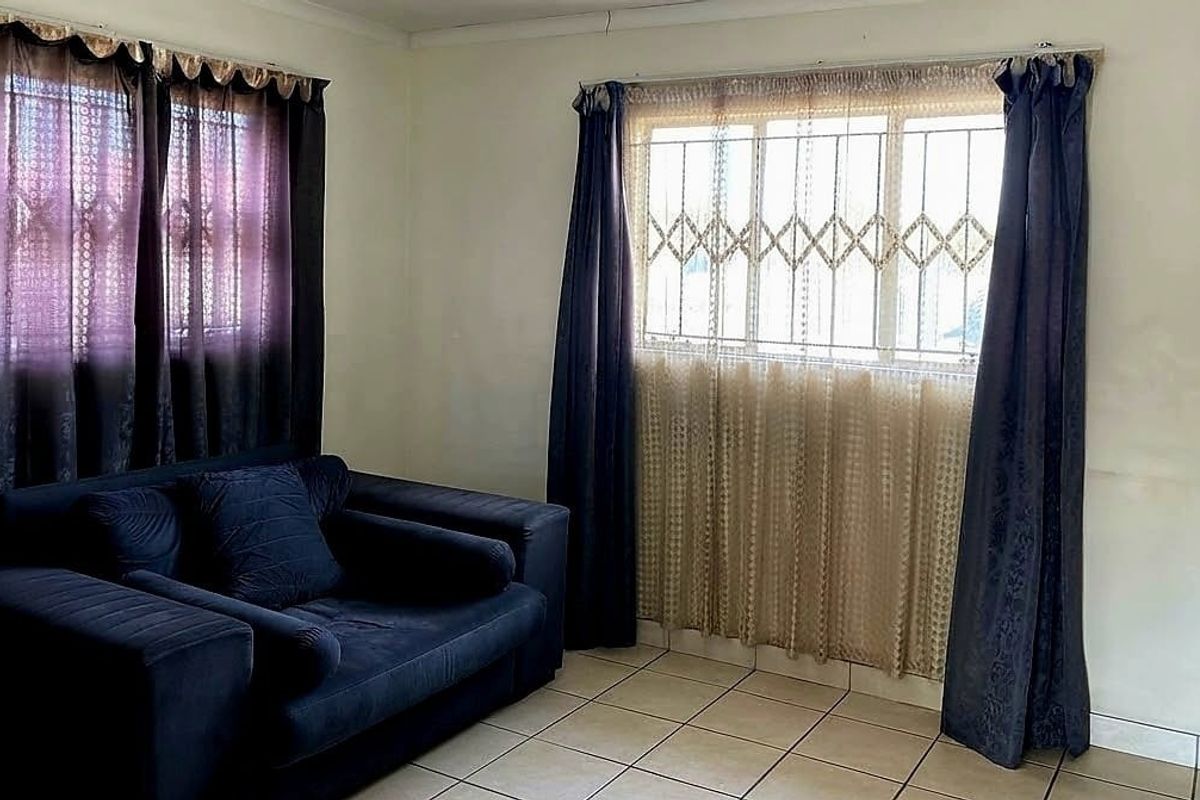 A living room featuring tiled flooring and windows fitted with security bars, showing signs of wear on the walls.