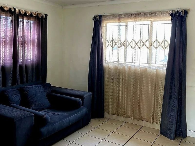 A living room featuring tiled flooring and windows fitted with security bars, showing signs of wear on the walls.