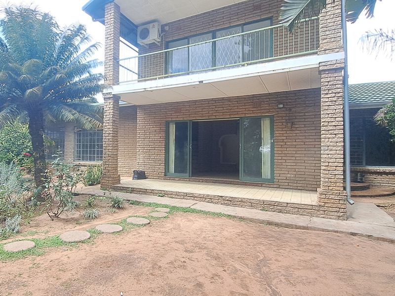 Rear view of a double-story brick house featuring a ground-floor patio, sliding glass doors, and an upper-level balcony with an installed air conditioning unit.