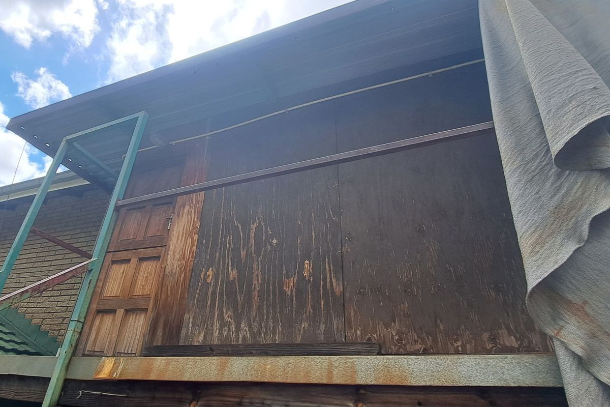 Rear exterior view showing a weathered timber facade and a corroded metal staircase attached to the brick building structure.