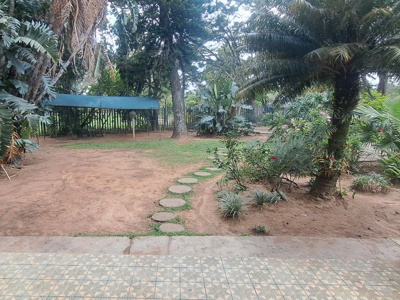 A spacious garden area featuring a tiled patio, a stepping stone path, mature landscaping, and perimeter fencing.