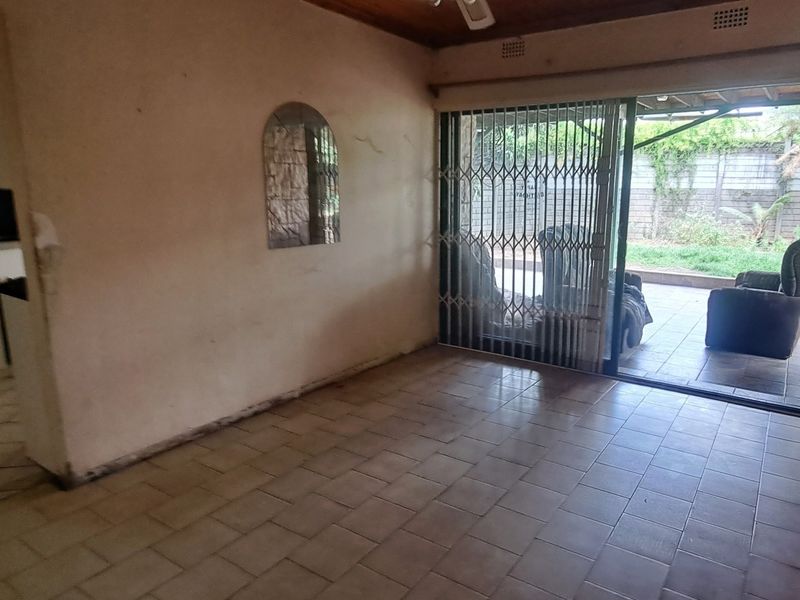 An empty living room featuring tiled flooring, a timber ceiling, and a sliding glass door with a security gate leading to the patio.