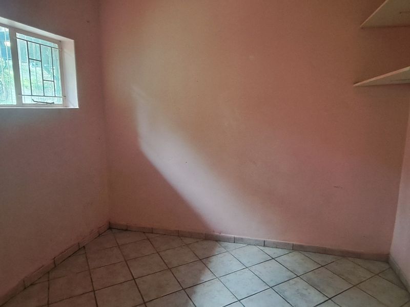 An empty bedroom featuring tiled flooring, built-in wall shelving, and a window fitted with security bars.